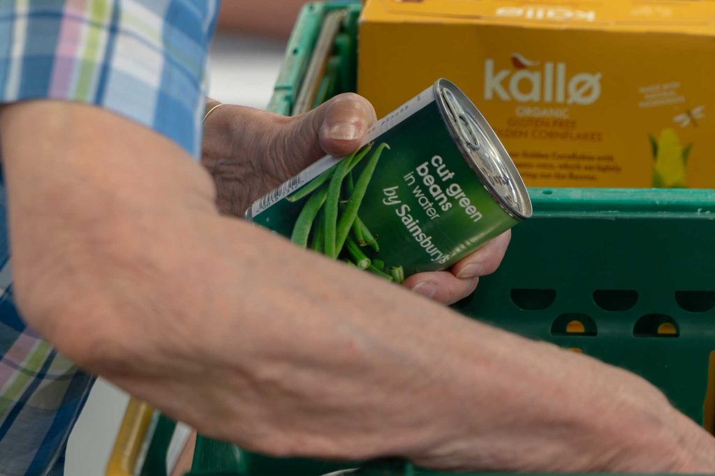 Lady packing a tin of Sainsbury's Green Beans into food bank box